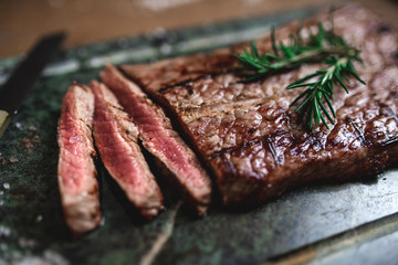 Close-up of sliced beefsteak cooked on the grill. Spiced with rosemary and coarse salt. Raw in the middle. Soapstone surface.
