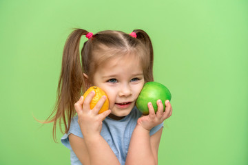 Fototapeta na wymiar little girl 4 years old in a blue T-shirt on a green background put an apple and a lemon to her face and smiles. pre-school children healthy eating concept