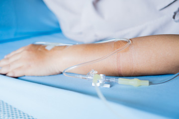 Patients saline, Iv drip, young woman hand with medical drip intravenous needle, give salt water on hospital bed. intravenous therapy (IV) is a therapy that delivers fluids directly into vein.