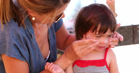 Mom applying sunscreen to upset child feeling angr