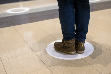 Closeup of feet of woman standing in the social distancing symbol on the floor in the train station...