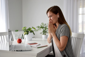 Woman in gray cardigan is sitting at the table near white laptop, notebook, phone and indoor...
