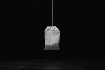 One tea bag hanging on a black background