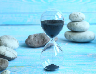 Close-up hourglass, measures the travel time in the countdown to the deadline, on a bright wooden blue background with copy space. Summer. The concept of summer holidays and travel. Time goes fast. 