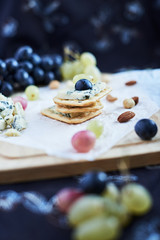 Three blue cheese crackers with grapes are on a cutting board.