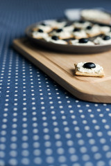 Plate with crackers with soft cheese and olives on a blue polka dot tablecloth.