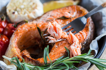 baked salmon steak with rosemary, lemon and spices in a black pan on a blue rustic background. Balanced diet
