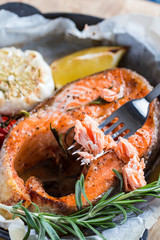 baked salmon steak with rosemary, lemon and spices in a black pan on a blue rustic background. Balanced diet
