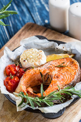 baked salmon steak with rosemary, lemon and spices in a black pan on a blue rustic background. Balanced diet