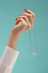 A female hand with red manicure is holding a silver chain with a pendant in the shape of a letter...
