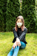 A teenage girl in a mask sits against a background of green trees.