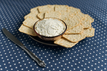 A plate with crackers and curd cheese lying on a polka dot tablecloth.