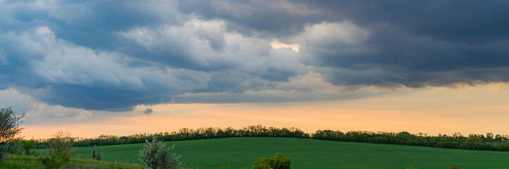 Green Grass Field on a Hill in the Background and a Bright dramatic sky in rural region