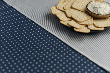 A plate with crackers and curd cheese lying on a polka dot tablecloth.