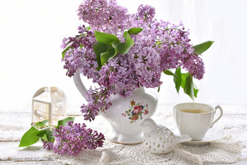 purple lilac blossoms in porcelain vase and cup of coffee on white table