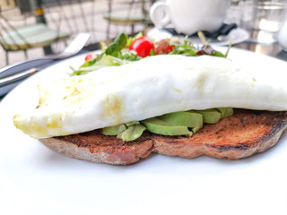 White omelet served with avocado slices on grilled bread toast with fresh lettuce and cherry tomatoes for side dishes ready to be eaten