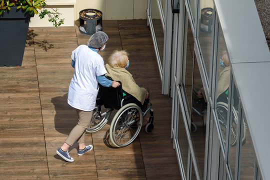 PARIS, FRANCE - MAY 13, 2020: nurse caring for an elderly and disabled woman in a nursing home on a sunny day during the coronavirus pandemic Covid-19. Both wear a protective face mask.