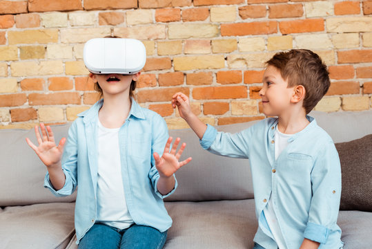happy brother looking at surprised sister in virtual reality headset - Powered by Adobe