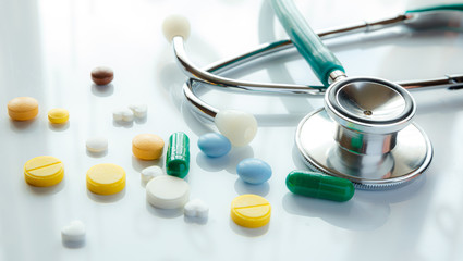 Stethoscope and multi-colored pills with reflection, medical concept