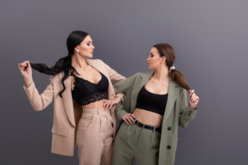 portrait of Two attractive business women wearing in suits and tops posing on grey background