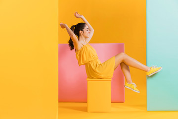 Happy woman in yellow dress sit very cheerful. Colorful creative yellow studio background.