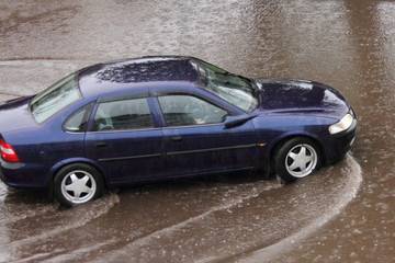Old German dark blue sedan car drives slowly through a large puddle, heavy rain in the city