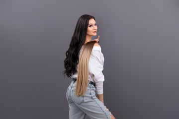 Fashion portrait of woman holding sections of hair for extension on grey background