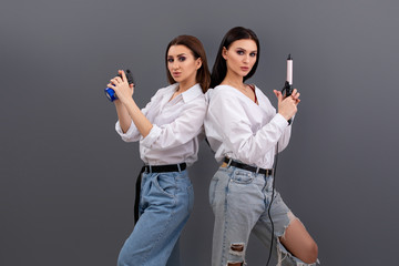buttle of two Professional hairdressers. Two hair stylists or artists holding spray and curling iron