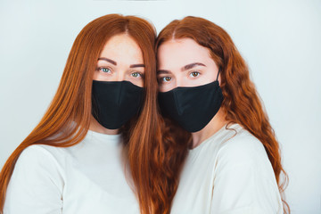 portrait of two redheaded young women both wearing black masks standing on isolated white...