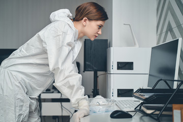 Beautiful young woman in protective suit using computer at work