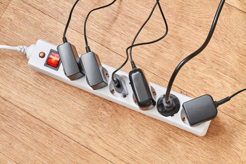 Electrical power strip overloaded with multiple electrical cords plugged in. Many plugs plugged into electric power bar
