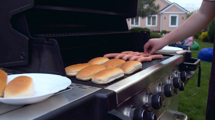 Person turning sausages for hot dog on grill