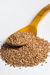 a handful of buckwheat and a wooden spoon above it. There is not much buckwheat on the spoon. Photo on a white background