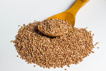 a handful of buckwheat and a wooden spoon above it. There is not much buckwheat on the spoon. Photo on a white background
