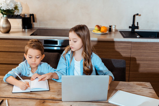 sister looking at brother writing in notebook near laptop while e-learning at home - Powered by Adobe