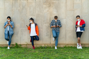 Teenagers texting mobile phone messages leaning on urban wall
