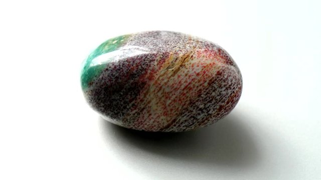 Natural multi-colored green red jasper stone Madagascar spins around its axis on a white stand and white background. Gems, minerals, collection of natural stones, close-ups, study of minerals