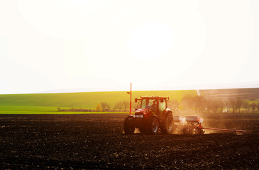 Fototapeta premium Farmer with tractor seeding sowing crops at agricultural fields in spring at sunset 