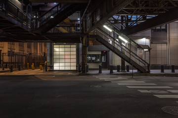 Wall of white panels with back-light behind a train stairwell leading to an urban subway loop in downtown Chicago at night