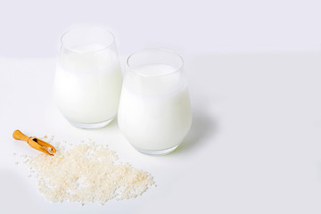 Two glass of vegatarian rice milk and rice grains on white background. Non dairy alternative milk. Concept of proper nutrition and healthy eating. Organic food. Copy space for text, selective focus