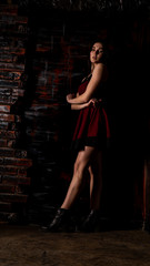Pretty young sexy model female with dark hair in amazing long red dress and black shoes posing in dark studio