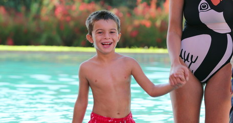 Happy Little boy pointing with finger to camera outside at the pool holding mother hand