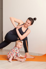 mother practices yoga at home with her child. Sport of a young mom with a toddler. Daughter...