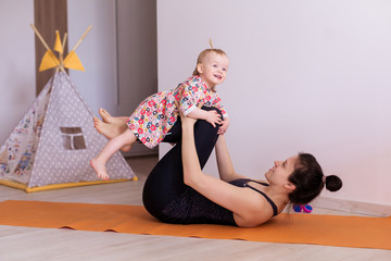 mother practices yoga at home with her child together. Sport of a young mom with a toddler....