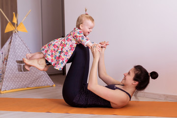 mother practices yoga at home with her child together. Sport of a young mom with a toddler....