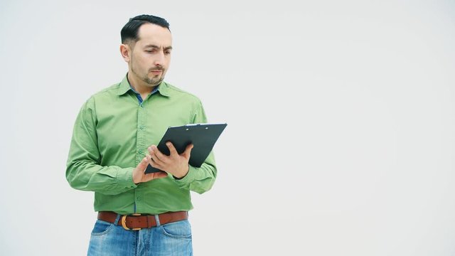 Funny young man holding a paper holder with writen on it question mark, watching surprisingly at at this mark and pointing his finger, showing to the camera, not understanding what it means.