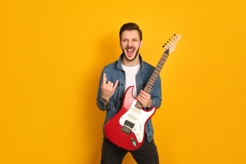 A portrait of crazy handsome musician holding electric guitar with one hand, shouting loudly,...