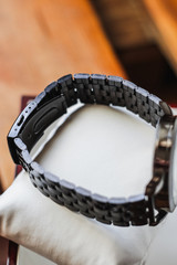 wrist watch with an open lock on a mitalic strap of a silver men watch back view. watch in a wooden box and on a white small pillow.