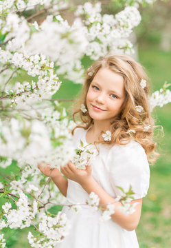 Portrait of a beautiful girl in a blooming garden in spring. Cute baby with white flowers in her hair.