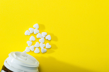 White pills in the form of a heart on a yellow background fall out of the jar, pharmaceuticals.